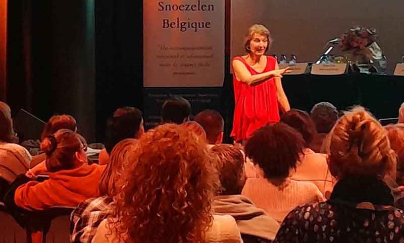 Une conférencière en robe rouge s'adresse à un auditoire attentif lors d'une conférence sur le bien-être.